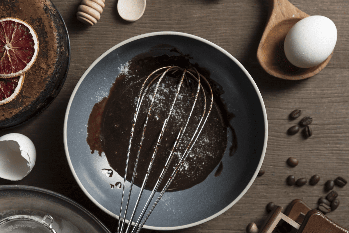 Brownie batter made with sweet potato, cashew butter, and cocoa powder in a mixing bowl with a whisk, egg on the side.